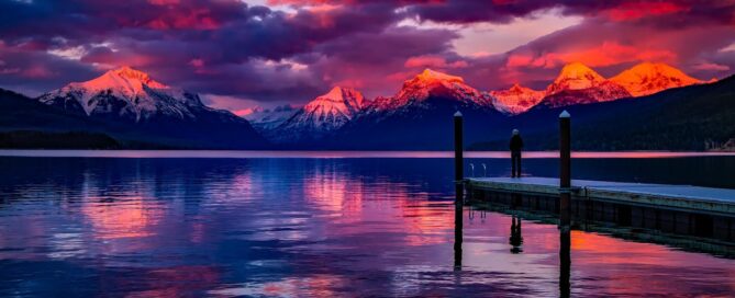 a purple, red and orange sunset on the water with a dock and mountains in the background